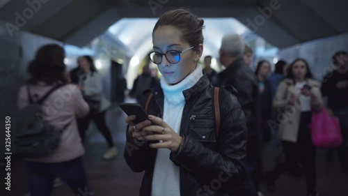 Woman standing in the entrance of a subway station using a smartphone while people walk around her