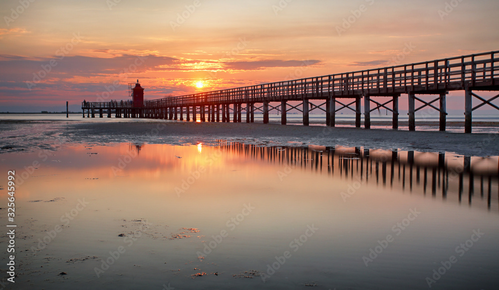 Wooden pier leading to a red lighthouse at sunrise in Lignano Sabbiadoro, Friuli, Italy - beach