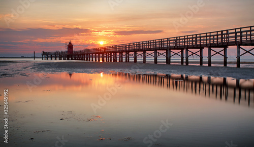 Wooden pier leading to a red lighthouse at sunrise in Lignano Sabbiadoro, Friuli, Italy - beach