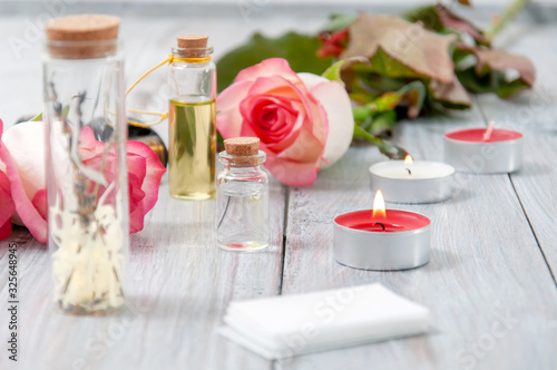 Pink roses  oil bottles and burning candles on a gray wooden table. March 8. Valentine s Day. Greeting card. Romantic and beautiful background. Spa treatments. Personal care. Love and beauty.