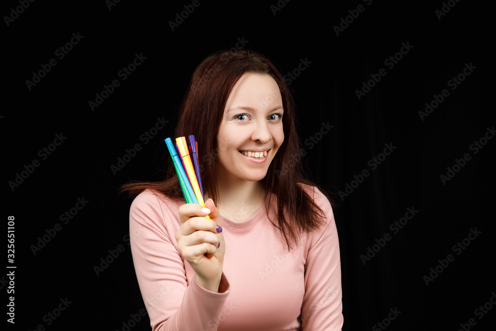 Cute woman holds markers or pens in her hand and shows on a black background. Copy space for text Cute woman holds markers or pens in her hand and shows on a black background. Copy space for text