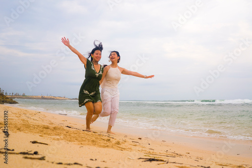 happy couple of attractive Asian Chinese women running crazy together at the beach enjoying holidays in gay lesbian love or close girlfriends relationship concept