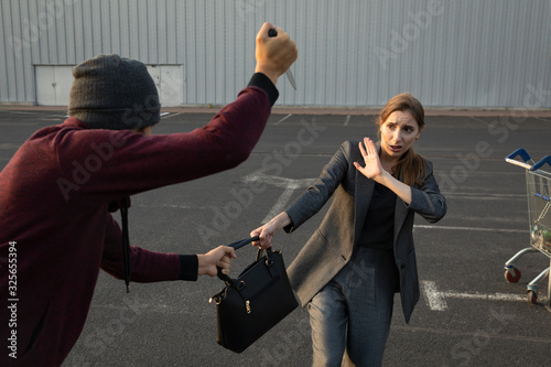 Quadro em tela A man attacked a defenseless woman in a parking lot, he is trying to take her purse from her