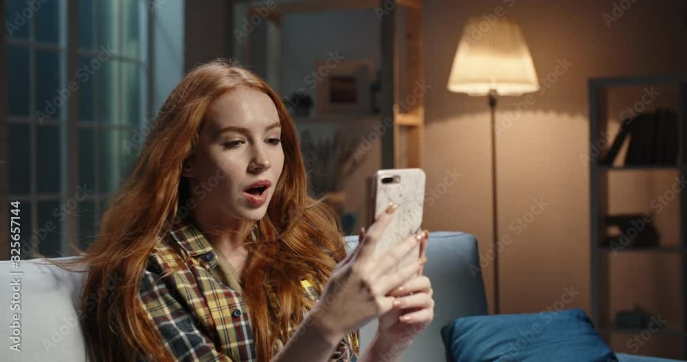 Astonished redhead caucasian girl looking at smartphone, wind blowing hair, Model reading breaking news, getting an amazing discount during online shopping or shocked by event 4k footage