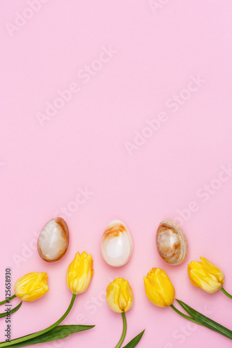 Easter pattern with blooming yellow flowers of tulip and eggs with stone texture. Decorative Easter eggs for holiday with copy space. Flat lay, vertical format.