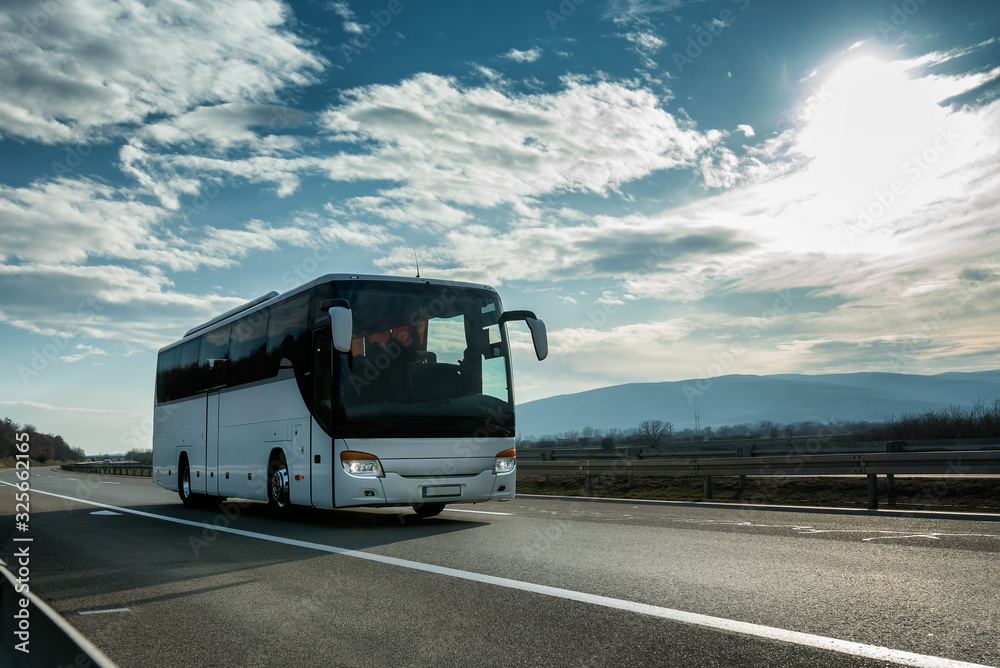 White Modern comfortable tourist bus driving through highway at bright sunny sunset. Travel and coach tourism concept. Trip and journey by vehicle