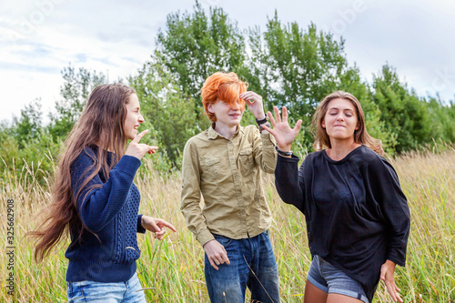 Summer holidays vacation happy people concept. Group of three friends boy and two girls dancing and having fun together outdoors. Picnic with friends on road trip in nature.