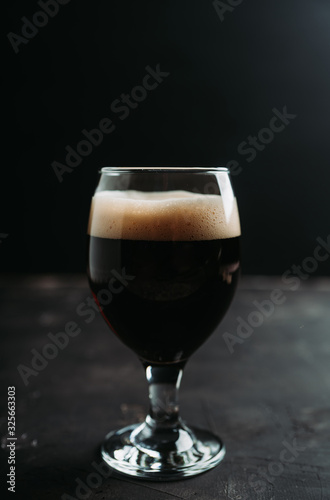 Freshly brewed dark beer on the black rustic background. Selective focus. Shallow depth of field.