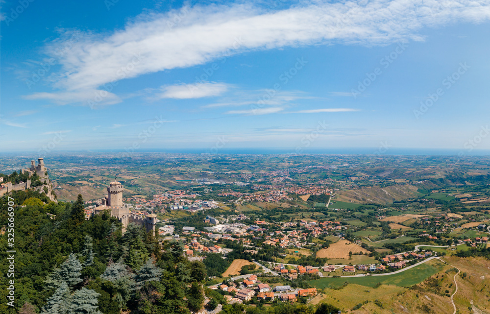 Aerial view on medieval fortress on top of the mountain, fortifications, in the background mountains and the city. The concept of the best places for tourism and holidays in Europe. San Marino, Italy Aerial view on medieval fortress on top of the mountain, fortifications, in the background mountains and the city. The concept of the best places for tourism and holidays in Europe. San Marino, Italy