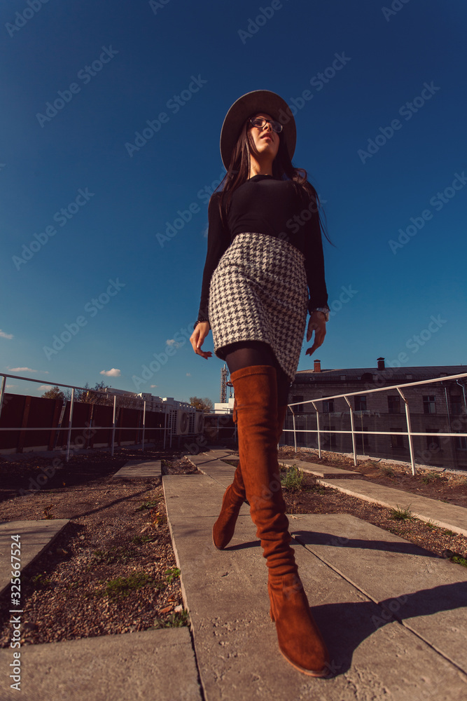 Young pretty stylish girl walking along the street. Girl model in hat walks along the street.