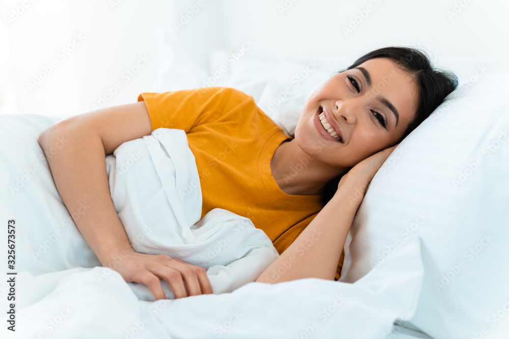 Happy positive young woman lies in bed indoors at home. Happy positive young woman lies in bed indoors at home.