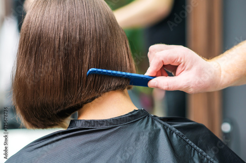 Closeup view hand and comb of hair dresser combing client's hair in salon.