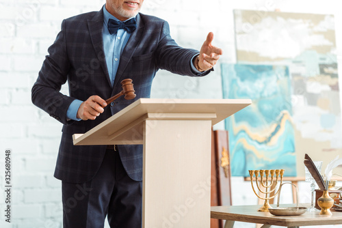 Foto cropped view of smiling auctioneer holding wooden gavel and pointing with hand d