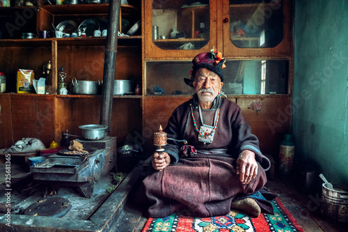 Portrait of an old man in typical tibetan clothes inside his house in Ladakh, Kashmir, India.