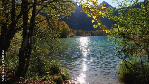 Sunny idyllic colorful autumn alpine view. Peaceful autumn Alps mountain lake with clear transparent water and sun reflections. Offensee lake, Salzkammergut, Upper Austria.
