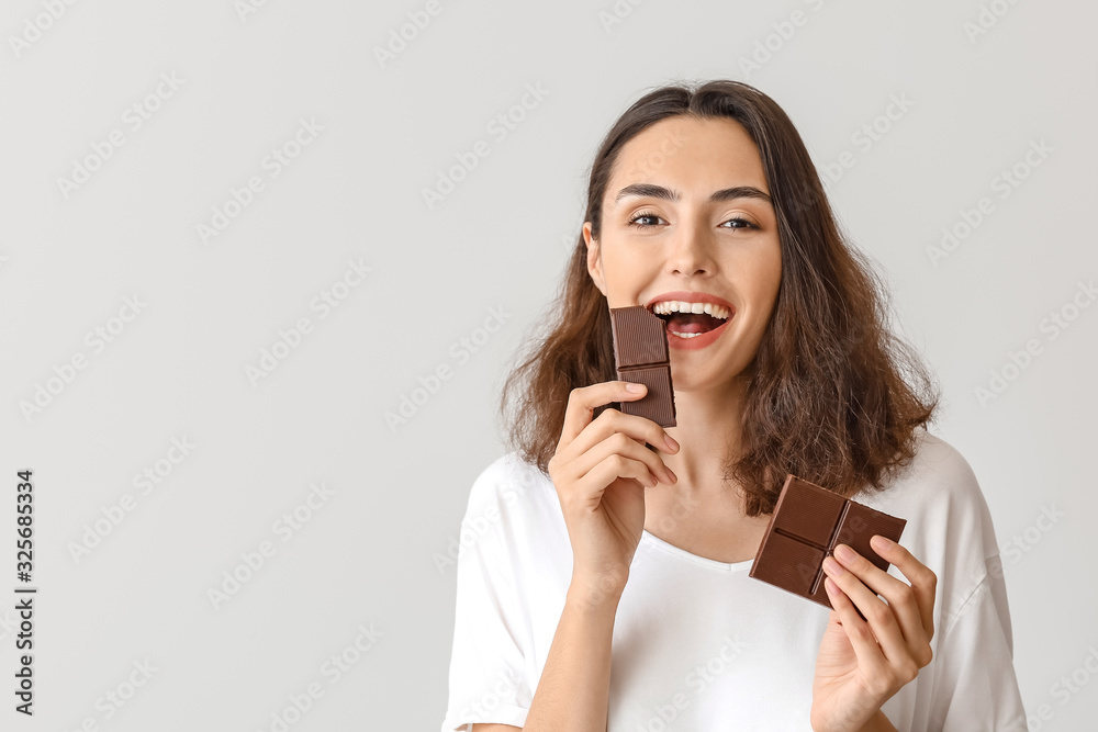 Beautiful young woman eating tasty chocolate on white background