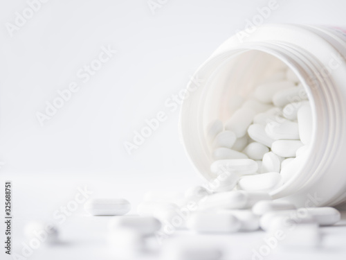 White pills spilled out of a plastic jar. Medicine capsules on white background with copy space.