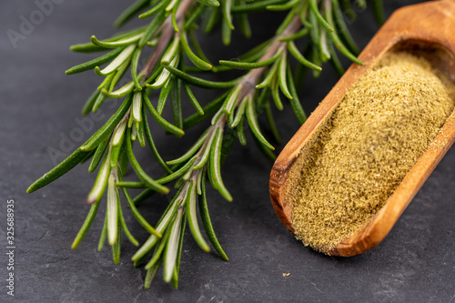 Extreme close-up view of fresh rosemary twigs and a spice shovel with ground rosemary on a black slate background