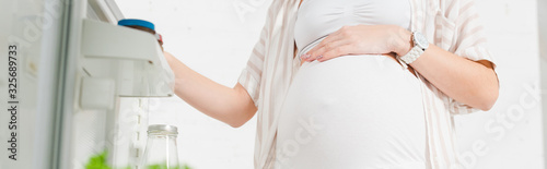 Cropped view of pregnant woman opening fridge door on white background, panoramic shot