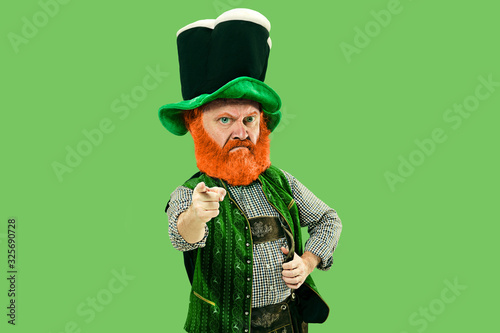 Pointing, choosing. Excited leprechaun in green suit with red beard on green background. Funny portrait of man ready for sales. Saint Patrick day, human emotions, celebration, traditional holidays. photo