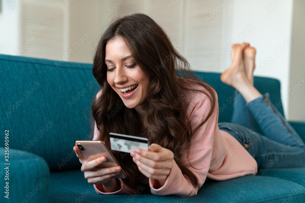 Woman using mobile phone holding credit card on sofa.