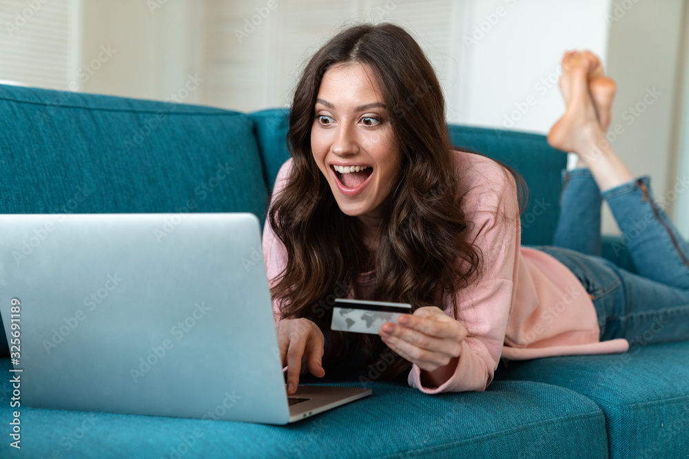 Emotional young woman holding credit card on sofa. Emotional young woman holding credit card on sofa.