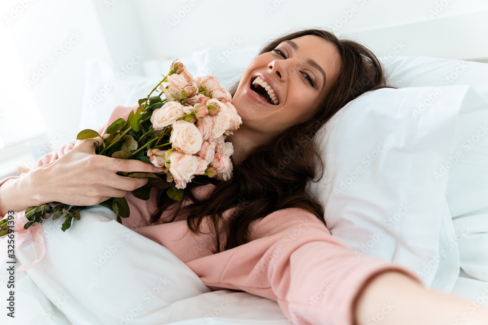 Pretty young woman in bed holding flowers.