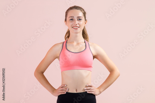 Happy young woman in fitness wear standing on pink background. Place for text. © A Stock Studio