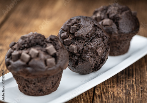 Old wooden table with fresh Chocolate Muffins (close-up shot; selective focus)