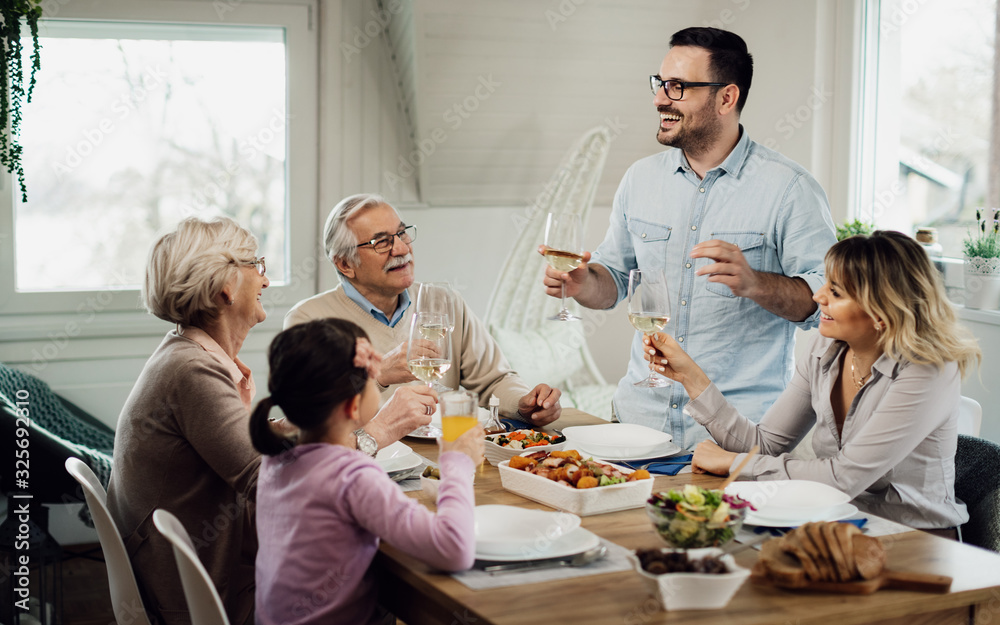 Happy man holding a toast while having lunch with his family at home. Happy man holding a toast while having lunch with his family at home.