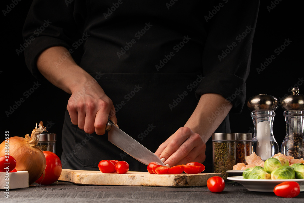 Chef cuts cherry tomatoes. Restaurant menu, cooking. On a black background, photo for advertising or design, restaurant business, cooking and recipe book.