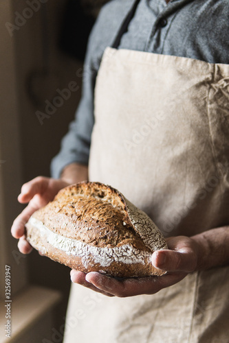 Stampa su tela Man in rustic apron holding a loaf of bread in his hands