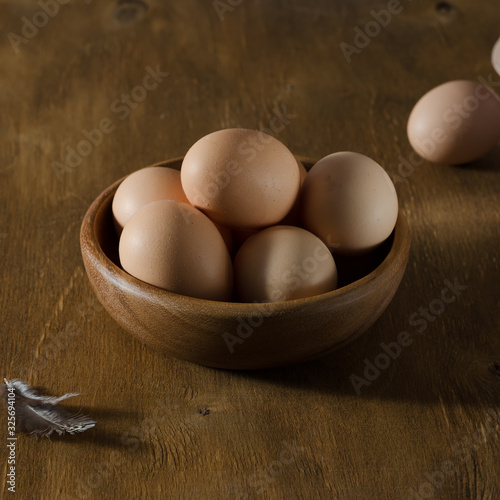 Wooden bowl with beige eggs on a wooden table.