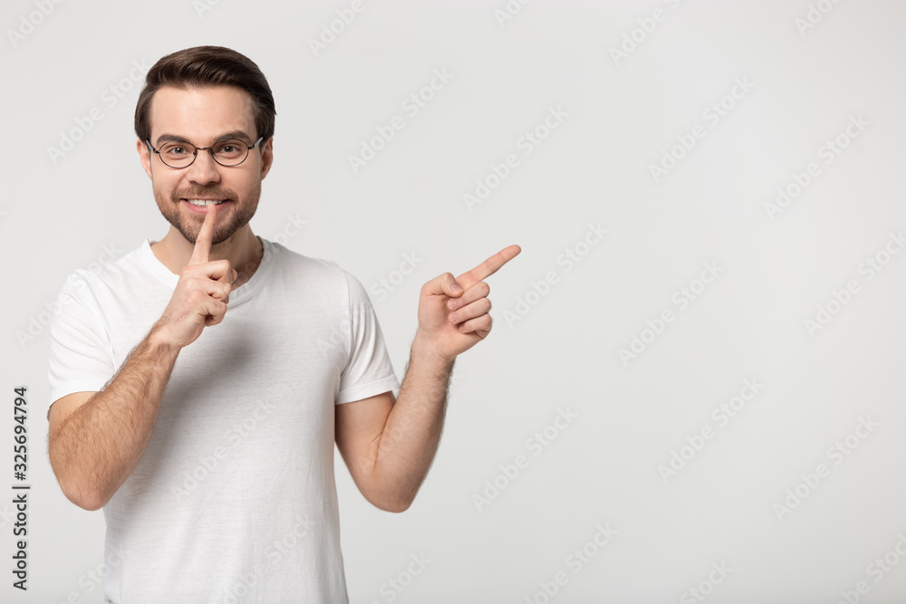 Happy guy making hush gesture, pointing aside on copy space. Happy guy making hush gesture, pointing aside on copy space.