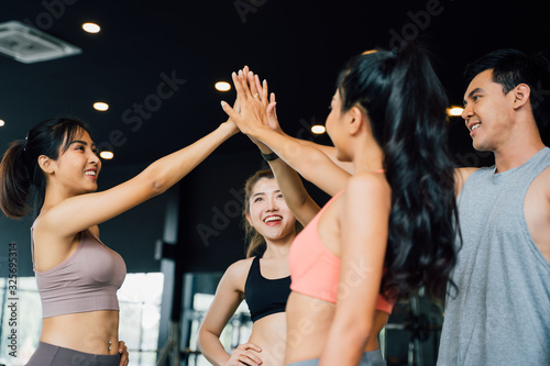 Smile man and women making hands together in fitness gym. Group of young people doing high five gesture in gym after workout. Happy successful workout class after training. Teamwork concept