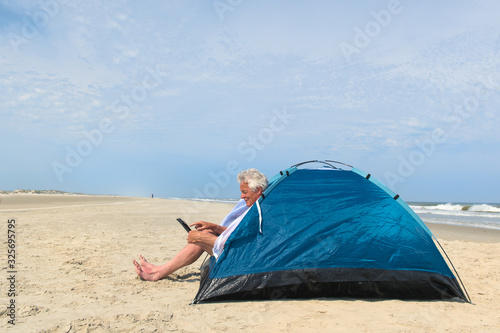 Man with digital tablet camping in shelter at the beach