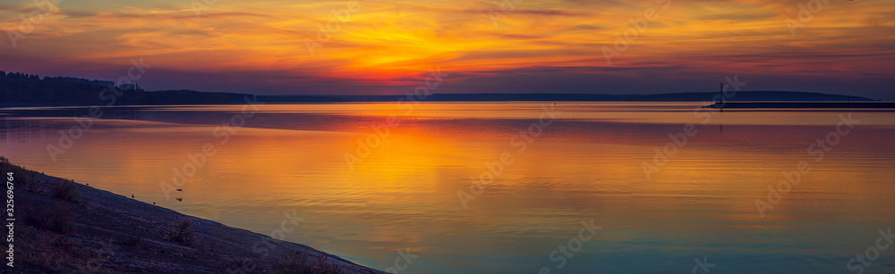 Panorama of colorful golden sunset over the Kremenchug water reservoir in Svetlovodsk city, Kirovograd region, Ukraine. Beautiful romantic sunset view of the sea with sun reflection on water