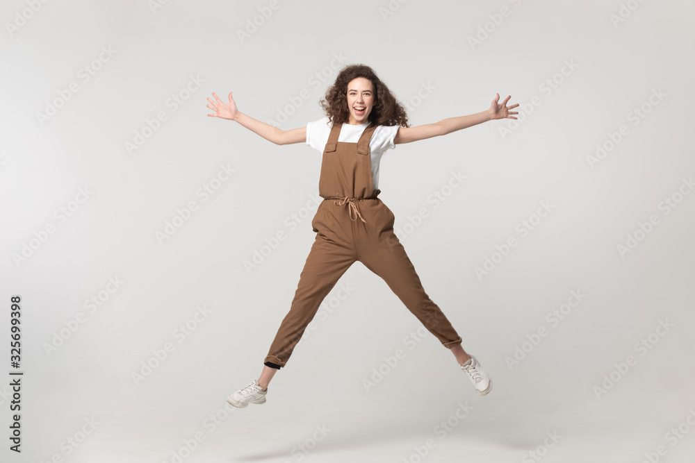 Excited young woman jumping with raised hands and straight legs.