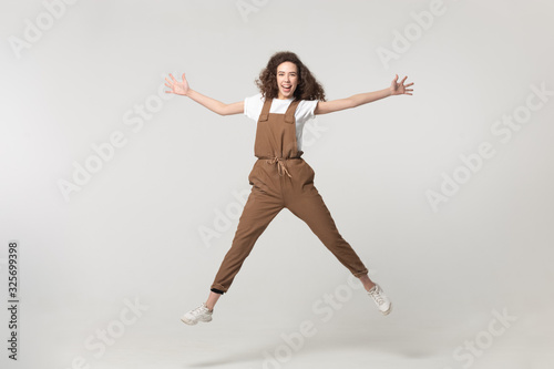 Excited young woman jumping with raised hands and straight legs.