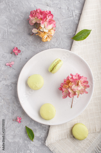Green macarons or macaroons cakes on white ceramic plate on a gray concrete background top view.