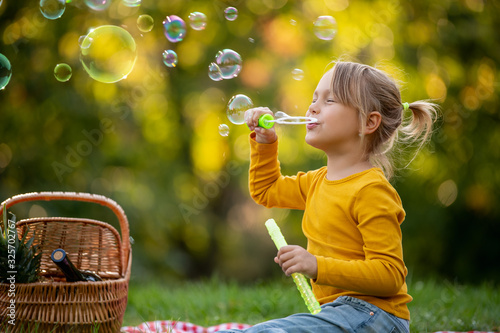 Happy little girl blowing soap bubbles in summer park