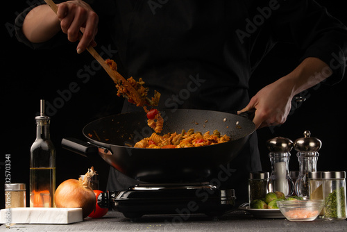 Cooking by the chef cook says Italian pasta with meat and vegetables, stirs, freezing in motion, on a black background.horizontal frame, restaurant business