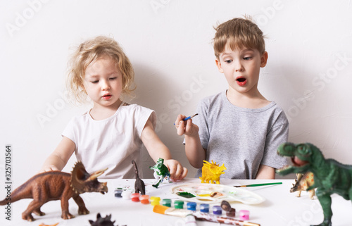 Children a boy and a girl are passionate and paint with figures and brush figures of toy dinosaurs. photo