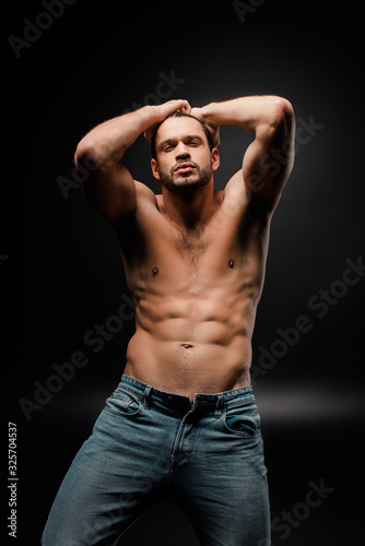 handsome and muscular man in jeans touching hair on black