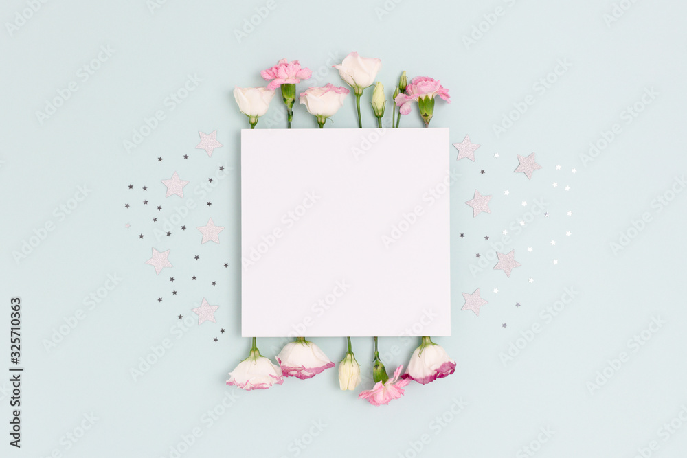 Blank paper card mockup with eustoma, carnation flowers and stars confetti. Festive concept with place for text on a blue pastel background.