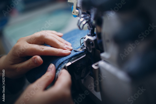 Young beautiful seamstress sews on sewing machine in factory