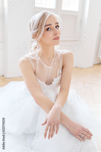 Blonde girl is sitting on the floor in a beautiful white wedding dress. A woman bride is waiting for the groom before the wedding © angel_nt
