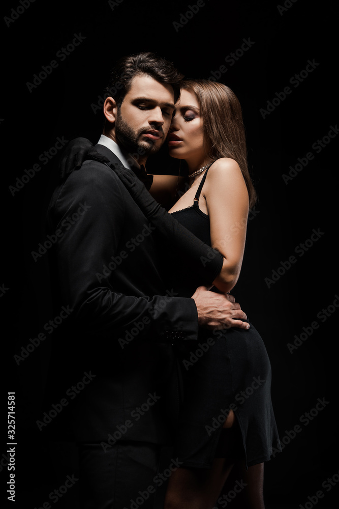 handsome man hugging attractive woman in dress isolated on black