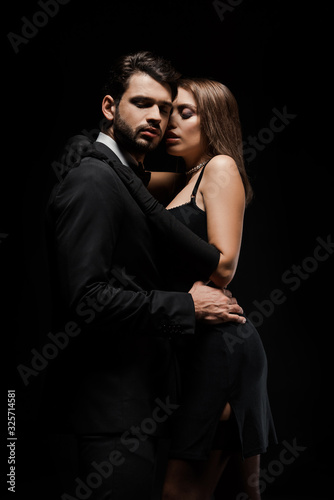 handsome man hugging attractive woman in dress isolated on black