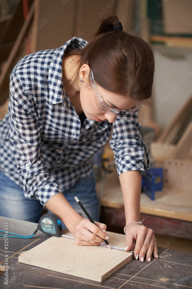 Young carpenter woman in glasses with tape measure and blackboard